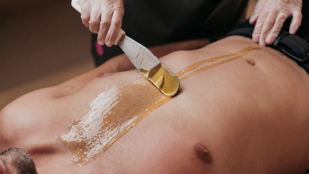 Profissional aplicando cera morna com mel e própolis no peito de um homem