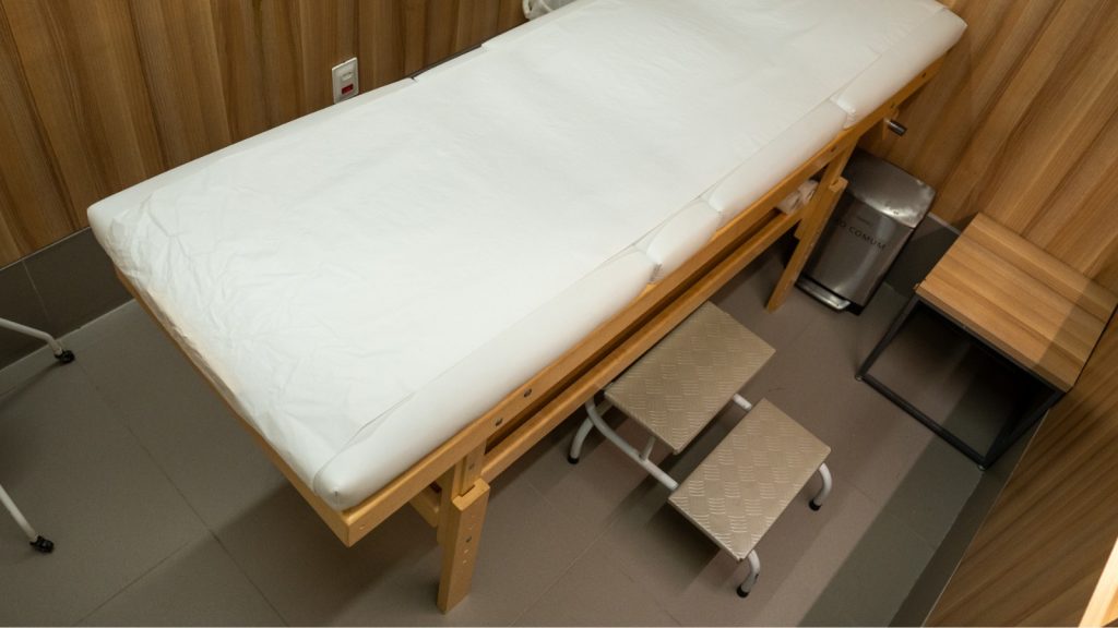 Cabine de depilação da Depyl Action com maca coberta por papel descartável e escada de apoio